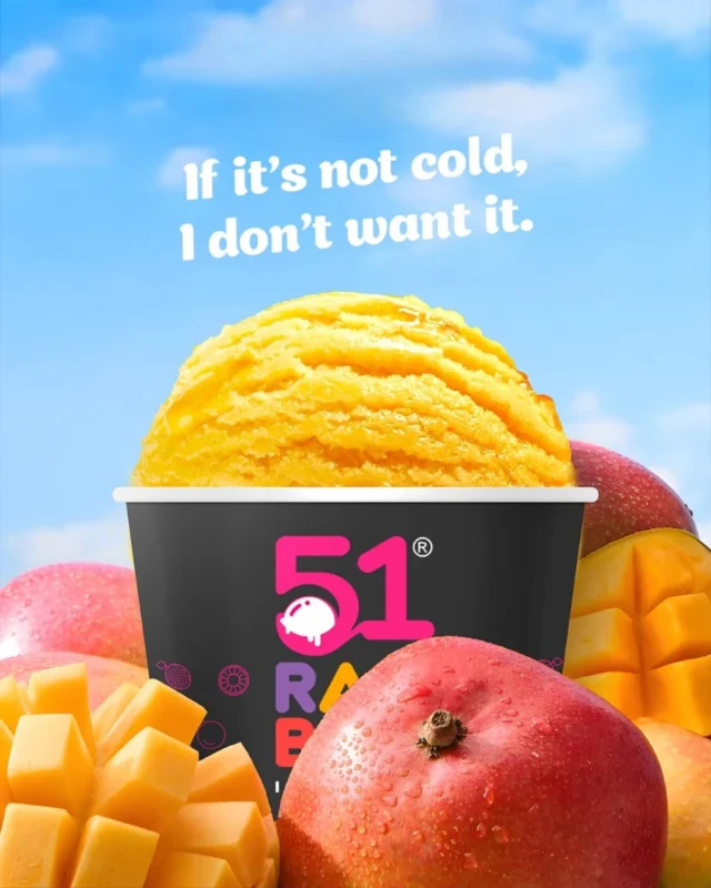 A vibrant scoop of mango ice cream surrounded by fresh mangoes in a 51 Rainbow cup