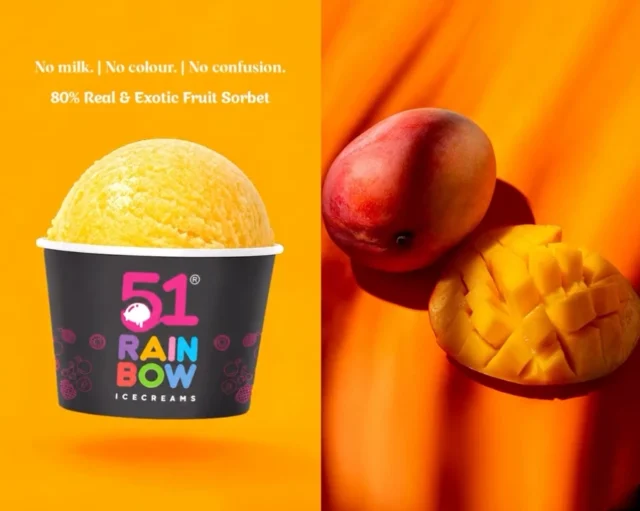 A bright golden mango sorbet scoop in a 51 Rainbow cup beside a halved fresh mango
